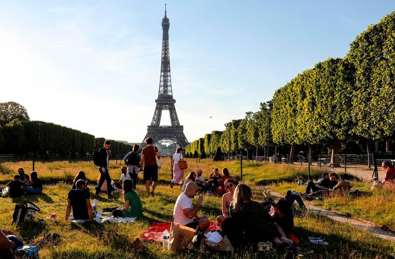 People sit on the Champs de Mars at sunset in front of the Eiffel Tower, on May 17, 2020, in Paris, on the first weekend after France eased lockdown measures taken to curb the spread of the COVID-19 pandemic, caused by the novel coronavirus.  / AFP / Ludovic MARIN
