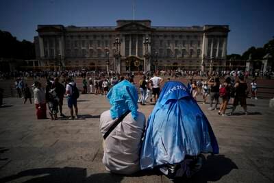 Visitors cover their heads from the sun after a scaled down version of the Changing of the Guard ceremony took place outside Buckingham Palace, during heavy heat in London. AP