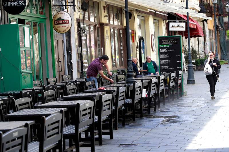 A Romanian washes the tables and the pavement of a beer terrace with as as another local passes by in Bucharest. EPA