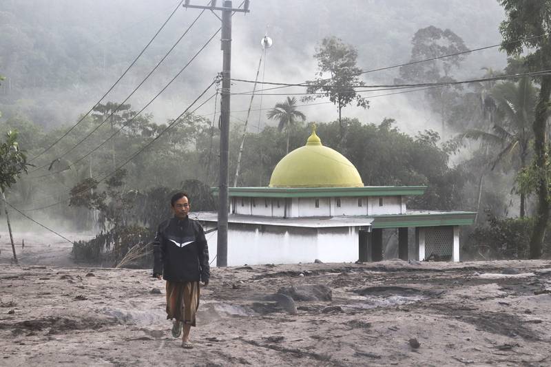 A man walks past a mosque partially covered in volcanic ash from the eruption of Mount Semeru in Kajar Kuning village. AP