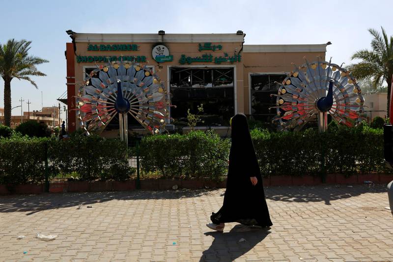 A woman walks past AlBasheer shopping centre, which was burnt by Supporters of Iraqi Shi'ite cleric Moqtada al-Sadr during an anti-corruption protest in Najaf, Iraq.  Reuters