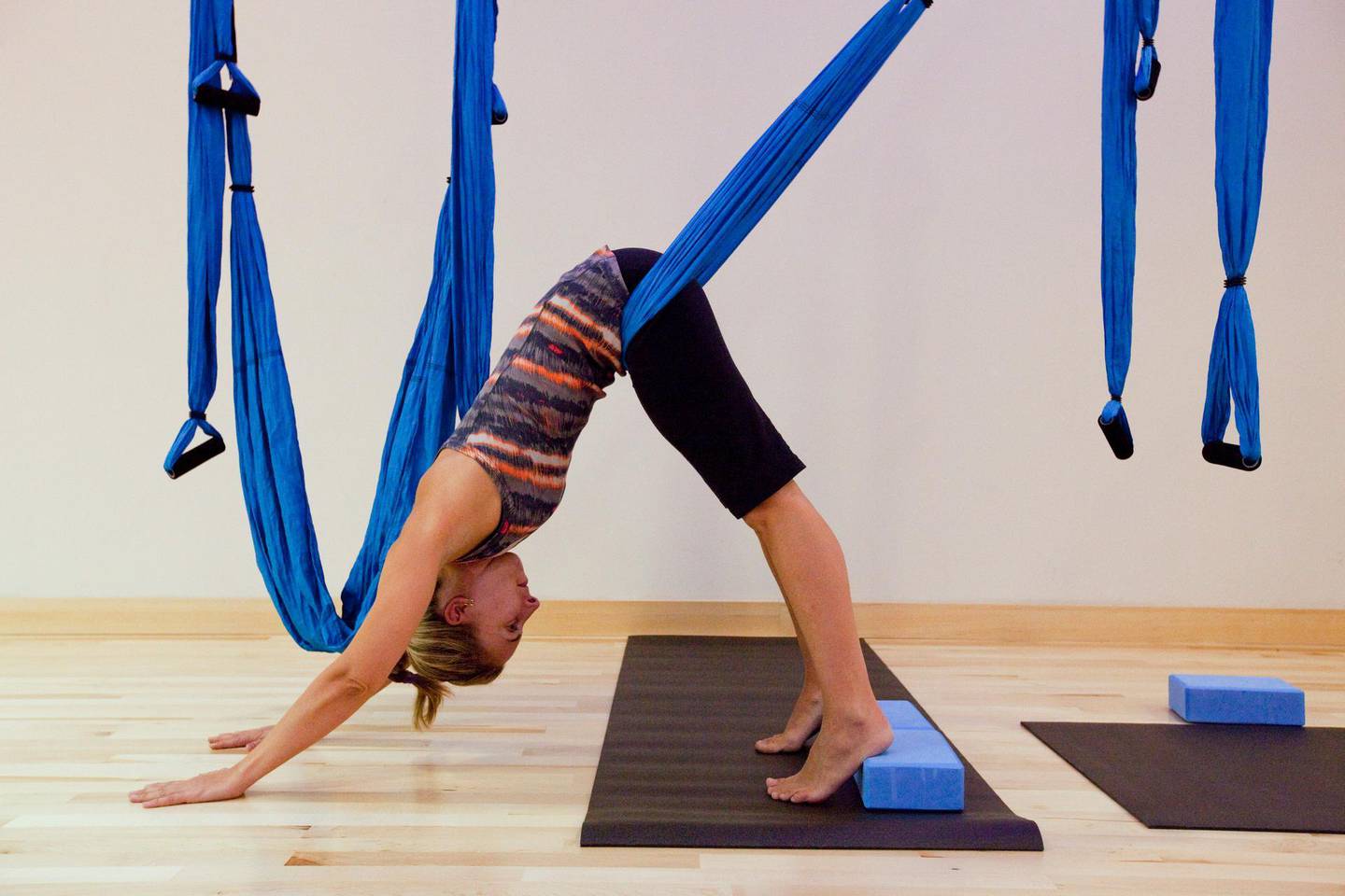 Dubai, United Arab Emirates - June 14 2012 - The National's Melanie Swan uses a  sling to push her deeper into downward dog at a Swing Yoga class at Fitness First in Dubai Motor City.  Swing Yoga is a form of yoga where students suspend themselves and conduct various poses with the help of a sling. The sling is made from parachute material and is suspended from the ceiling using rock climbing carabiners. Slings help move yoga students deeper into poses and allow for easier inversions. (Razan Alzayani / The National) 