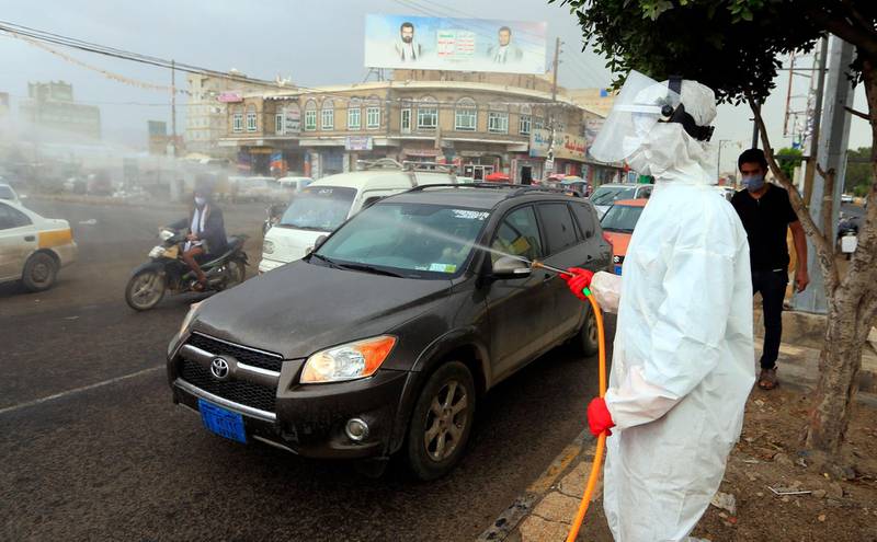A Yemeni worker wearing a protective outfit sprays disinfectant on passing cars and motorcycles in the capital Sanaa, during the ongoing novel coronavirus pandemic crisis, on May 21, 2020. / AFP / Mohammed HUWAIS
