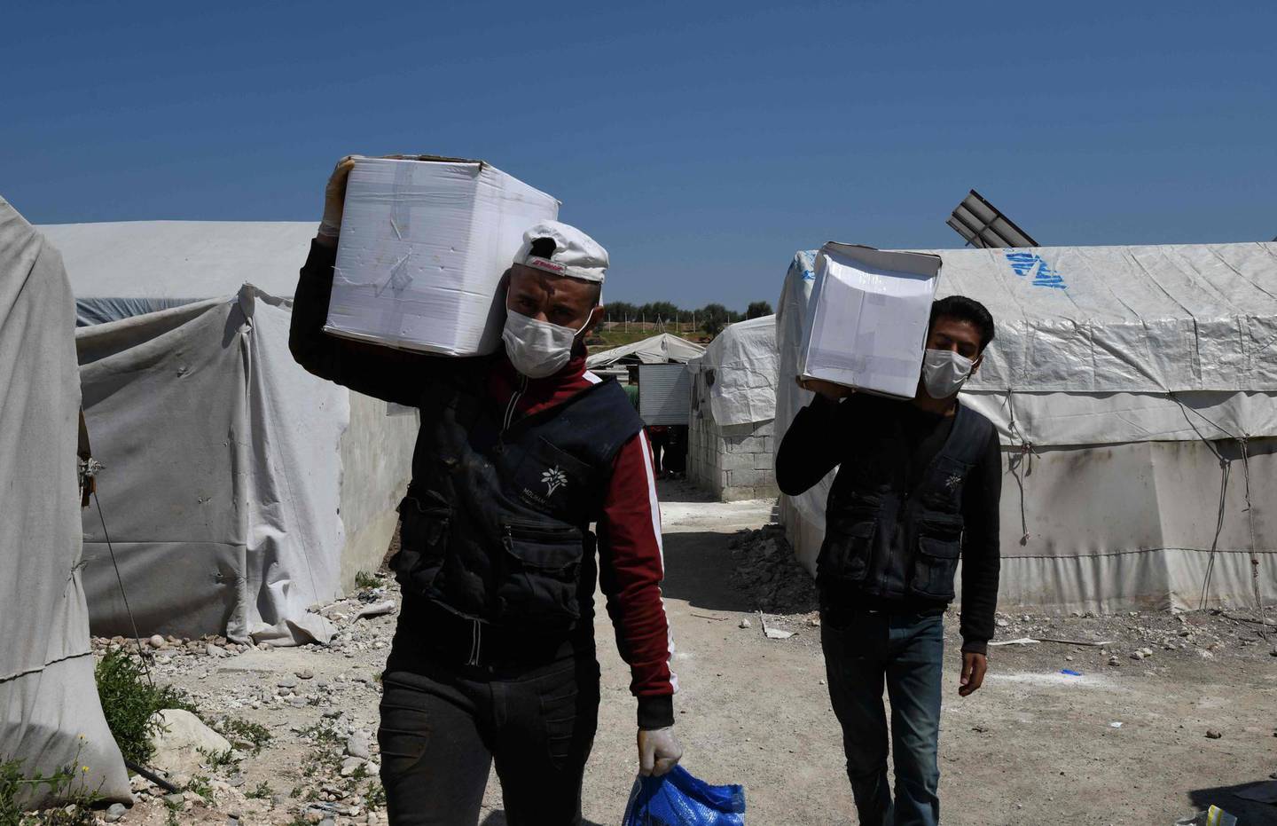 Volunteers deliver aid at a camp for displaced Syrians near the town of Deir al-Ballut, by the border with Turkey, in Syria's Afrin region in the northwest of the rebel-held side of the Aleppo province on April 14, 2020 during the coronavirus COVID-19 pandemic. / AFP / Rami al SAYED
