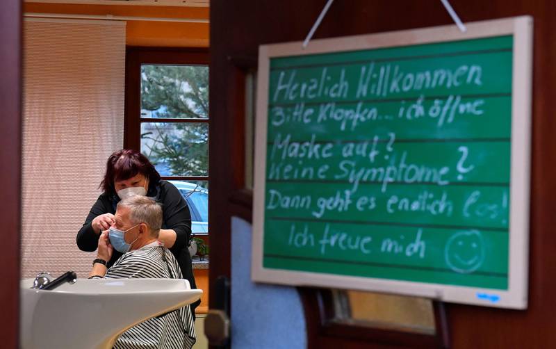 Hairdresser Manuela Friedl cuts their hair of a customer in Haselbachtal. The sign reads: "Sincerely welcome, please knock - I will open, wear a mask? no symptoms? Now it finally starts, I am happy". Reuters