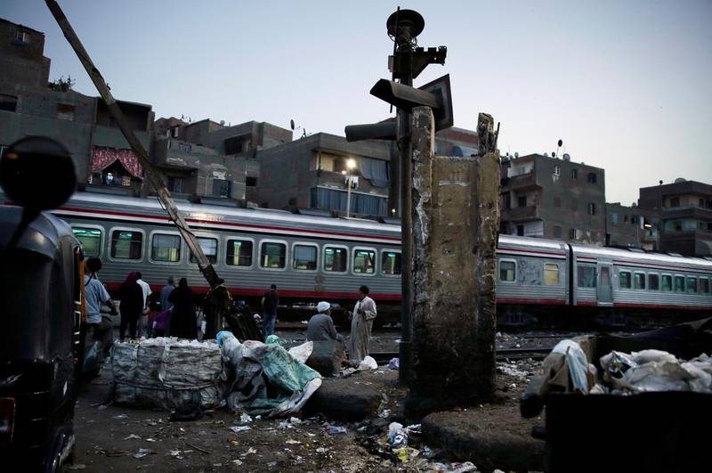 FILE - In this Oct. 23, 2018 file photo, people wait for the train to pass in Shubra, Cairo, Egypt. An Egyptian train conductor who forced two poor street vendors without tickets to jump off a moving train, leading to the death of one of the youths, has been arrested, authorities said Tuesday, Oct. 29, 2019. Egyptâ€™s railway system has a history of badly maintained equipment and poor management. (AP Photo/Nariman El-Mofty, File)