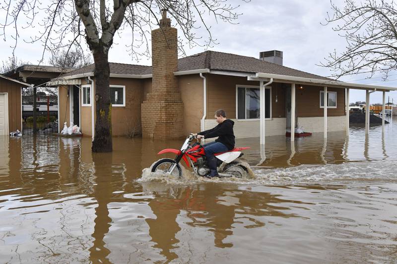 A child rides his off-road motorcycle around his flooded home in Brentwood. AP