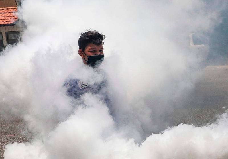 A mask-clad Palestinian boy is seen through the fumes from a Hebron municipality vehicle fumigating a street in the city of Hebron in the occupied West Bank, after a recent surge of coronavirus cases.   AFP