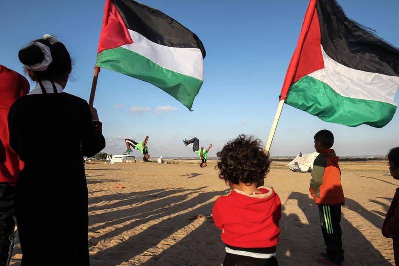 Palestinians hold their national flag as youths practice their parkour skills at the Israel-Gaza border in the southern Gaza Strip. Said Khatib / AFP