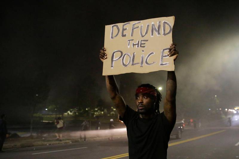 A man holds up a sign amid smoke of a fire during a protest Saturday, June 13, 2020, near the Atlanta Wendy's where Rayshard Brooks was shot and killed by police. AP