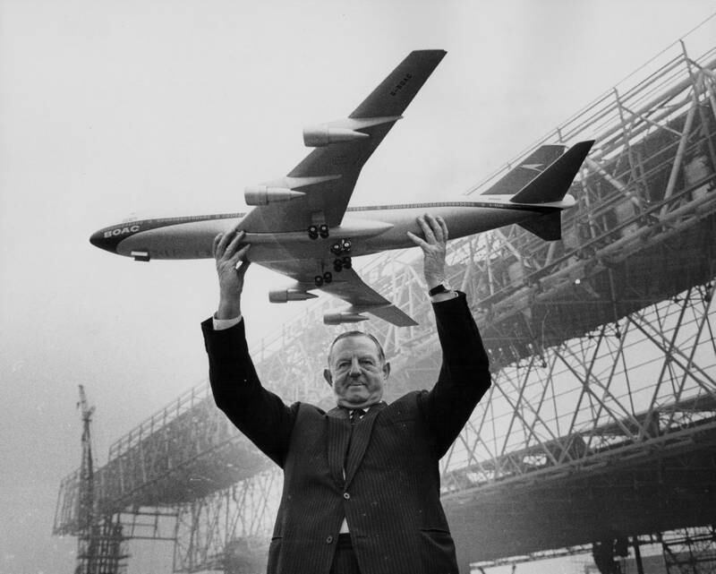 Keith Granville, managing director of BOAC, holding up a model of the Boeing 747 jet, with the new aircraft hangars under construction in the background, at Heathrow in 1969.