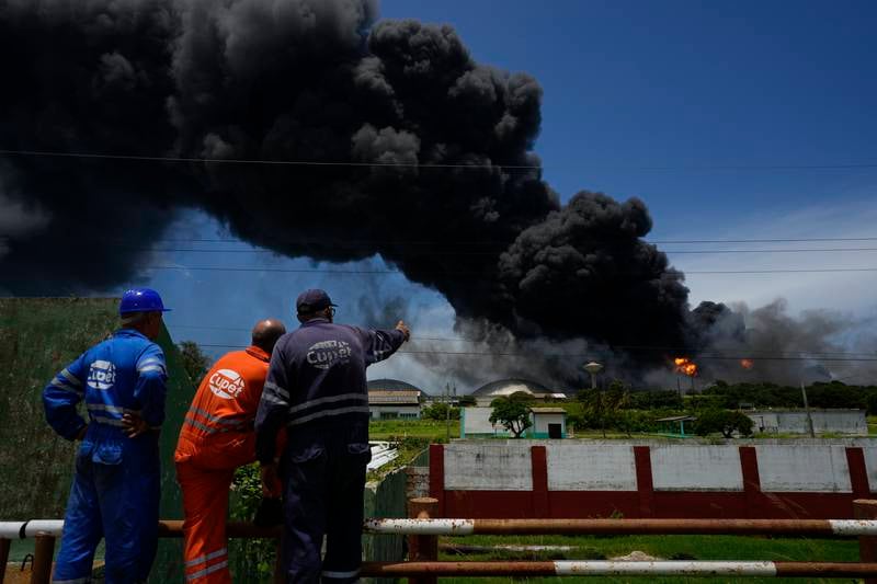 Workers watch a huge plume of smoke rising from the Matanzas depot. The Cuban authorities say lightning struck a crude oil storage tank at the base, causing a fire that led to four explosions. AP