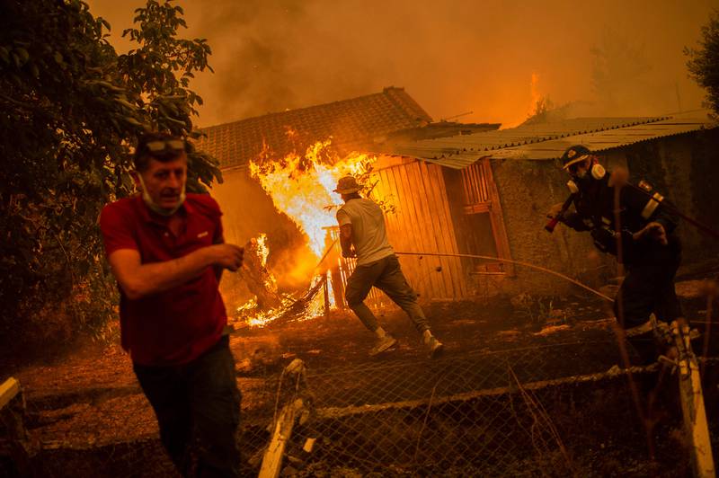 A firefighter and locals rush to a burning house in an attempt to extinguish fires approaching  Pefki.