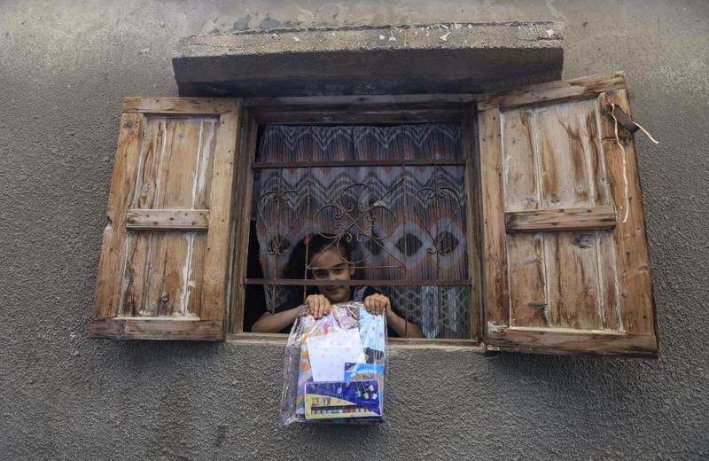 A Palestinian girl at her window displays a package of crafts and reading material distributed by volunteers for the Women's Program Center to children in confinement due to the novel coronavirus pandemic, in the central Deir al-Balah refugee camp in the Gaza Strip, on April 12, 2020. (Photo by MAHMUD HAMS / AFP)