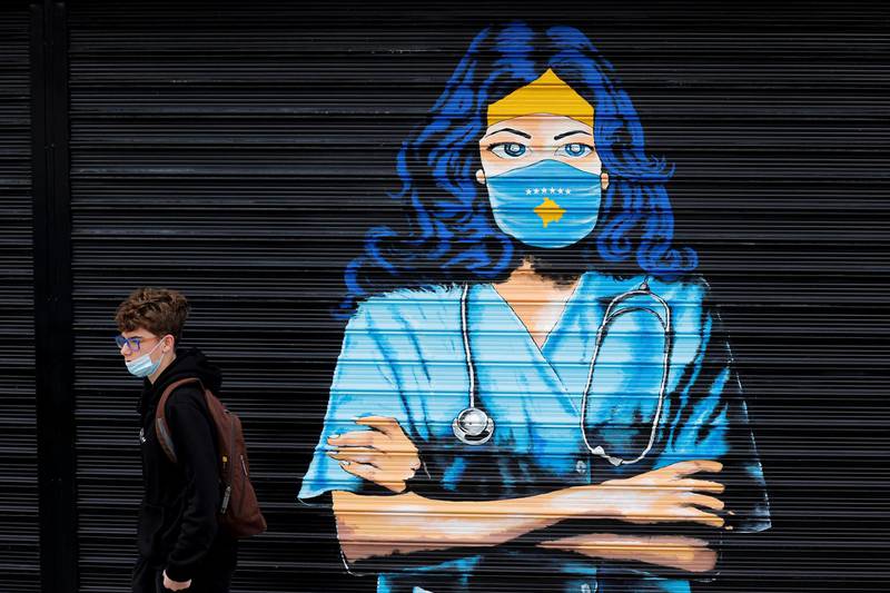 A boy wearing face mask walks by a mural depicting a nurse in Pristina, Kosovo. EPA