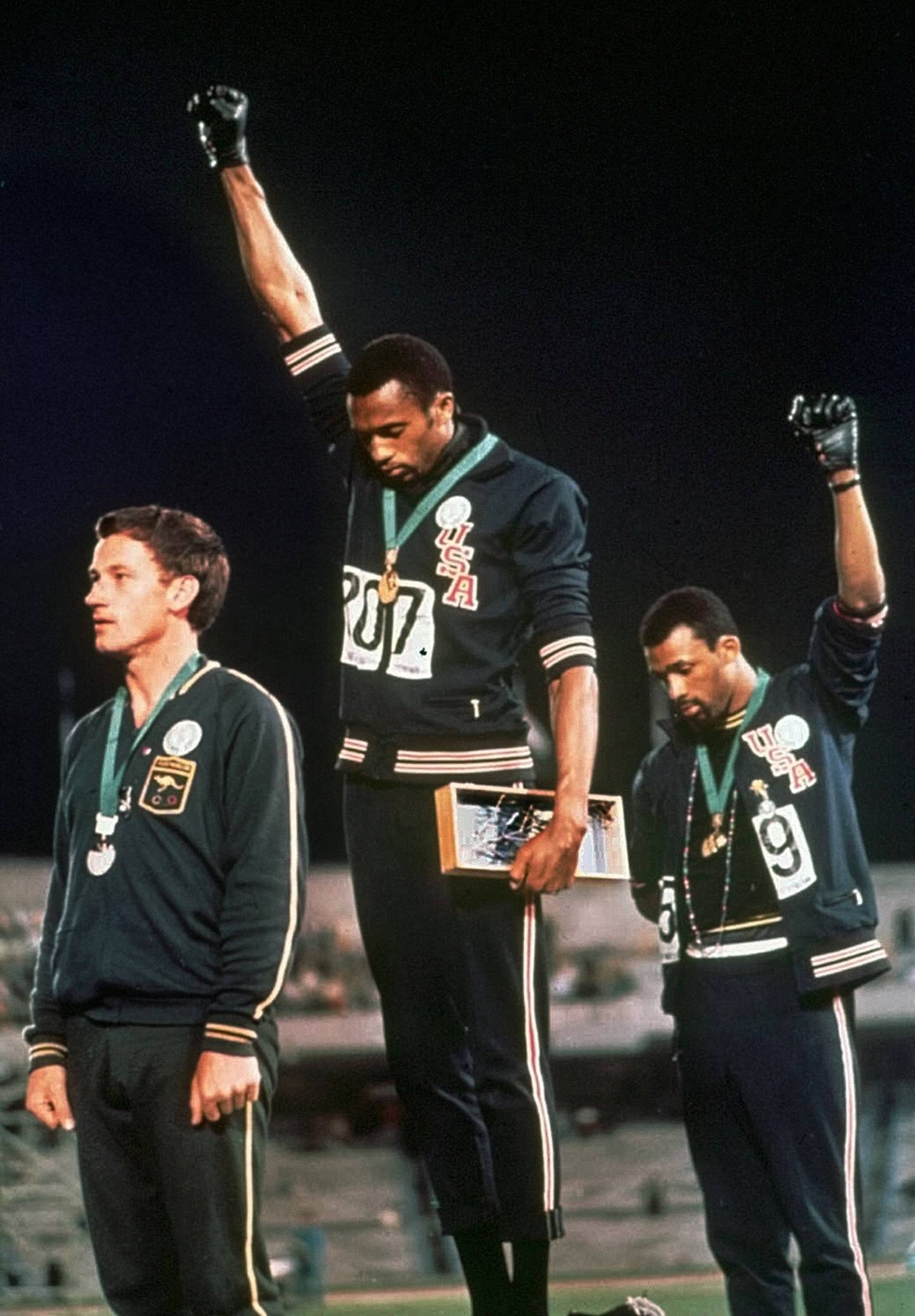 US athletes Tommie Smith, center, and John Carlos stare downward and extend gloved hands skyward in a Black power salute after Smith received the gold and Carlos the bronze for the 200 meter run at the Summer Olympic Games. Australian silver medalist Peter Norman is on the left, October 16, 1968, in Mexico City. AP