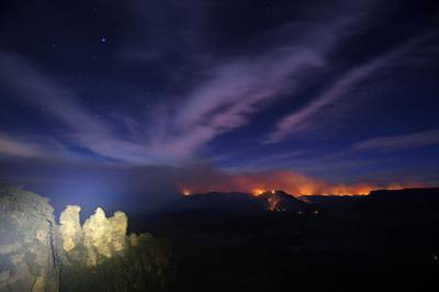 A long exposure photograph shows the Three Sisters rock formation as flames from the Kowmung River fire and the Green Wattle Creek fire are visible from Echo Point lookout in Katoomba, New South Wales, Australia.  EPA