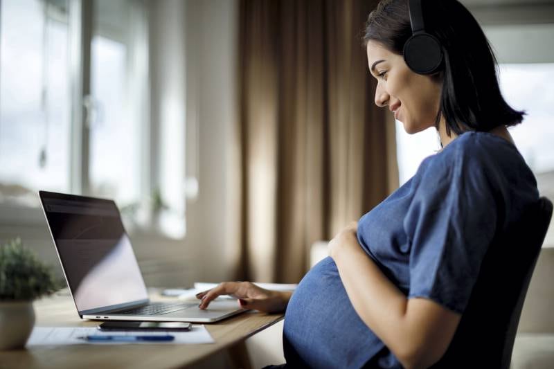 Pregnant woman with headphones using laptop