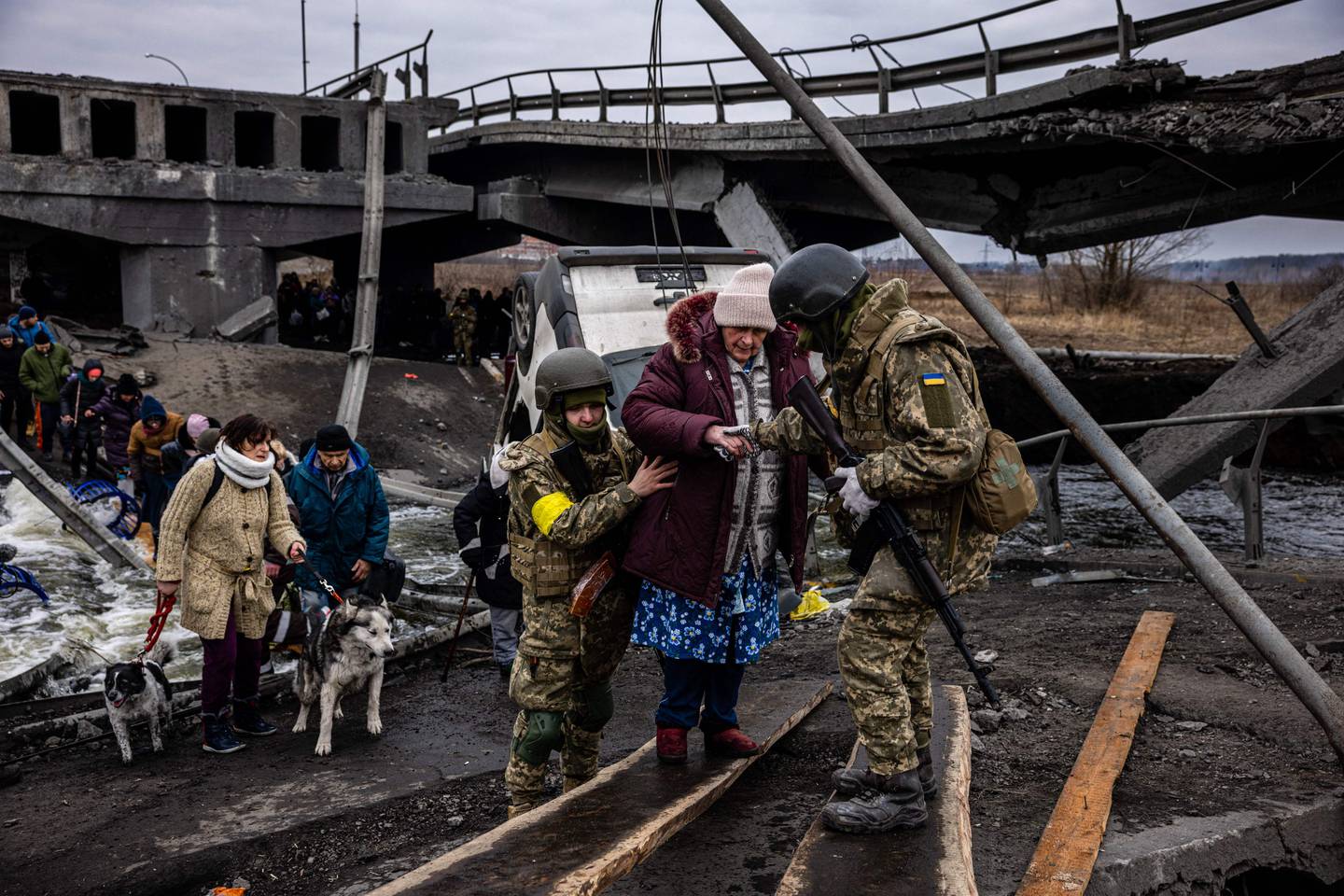 Ukrainian soldiers help an elderly woman to cross a damaged bridge as she flees from Irpin, north-west of Kyiv, on Monday. AFP