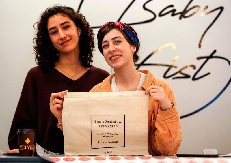 Palestinian fashion designer and label founder Yasmeen Mjalli (L), along with her creative director Amira Khader, pose for a picture with one of their label "BabyFist's" canvas bags in their shop in Ramallah in the occupied West Bank on December 19, 2018. It's only three words on a T-shirt or embroidered on a denim jacket, but they carry a powerful message: "Not you habibti (darling)." "BabyFist" label founder Yasmeen Mjalli, 22, sees the clothes helping to empower Palestinian women facing unwelcome male attention in public, placing on the fabrics of muted colours and on canvas bags messages in English and Arabic inside drawings of flowers and other designs. / AFP / ABBAS MOMANI
