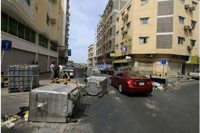 Cars pass garbage containers thrown onto the road to prevent riot police from entering the street in the centre of Manama.