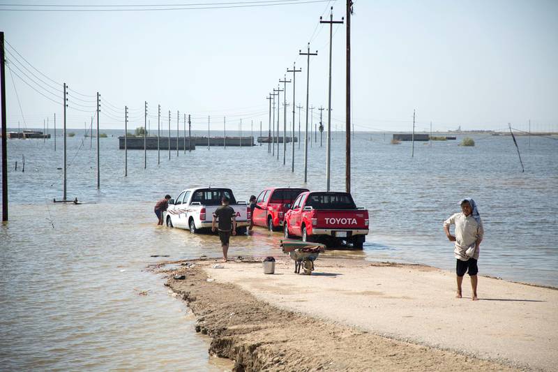 Vehicles sit at the edge of a flooded area in southern Iraq's al-Qurna district, north of Basra, on April 10, 2019. - Weeks of rain -- compounded by melting snowcaps in neighbouring Turkey and Iran -- have almost filled Iraq's four central reservoirs and swelled its two main rivers, the Tigris and Euphrates. (Photo by Hussein FALEH / AFP)
