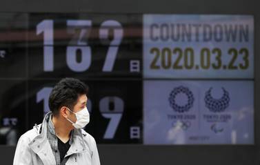 A passersby, wearing a face mask, walks past a screen counting down the days to the Tokyo 2020 Olympic Games in Tokyo. Reuters