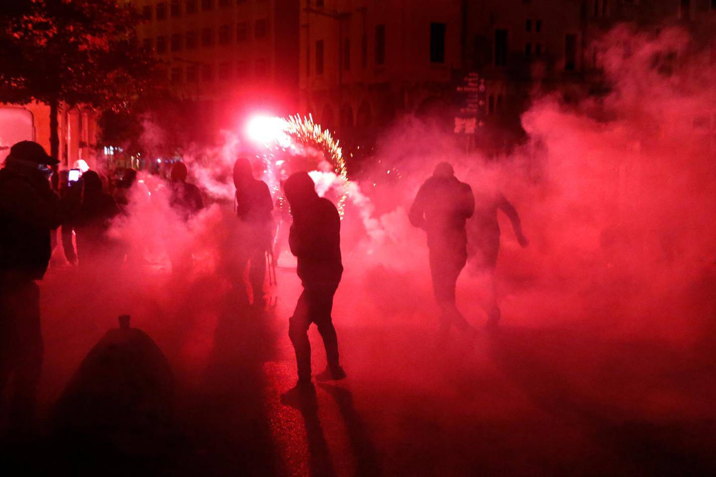 Anti-government protesters are covered by tear gas smoke, as they throw firecrackers against the riot police, during ongoing protests against the political elites in Beirut, Lebanon, Saturday, Jan. 18, 2020. Riot police fired tear gas and sprayed water cannon near parliament in Lebanon's capital Saturday to disperse thousands of protesters after riots broke out during a march against the ruling elite amid a severe economic crisis. (AP Photo/Hussein Malla)