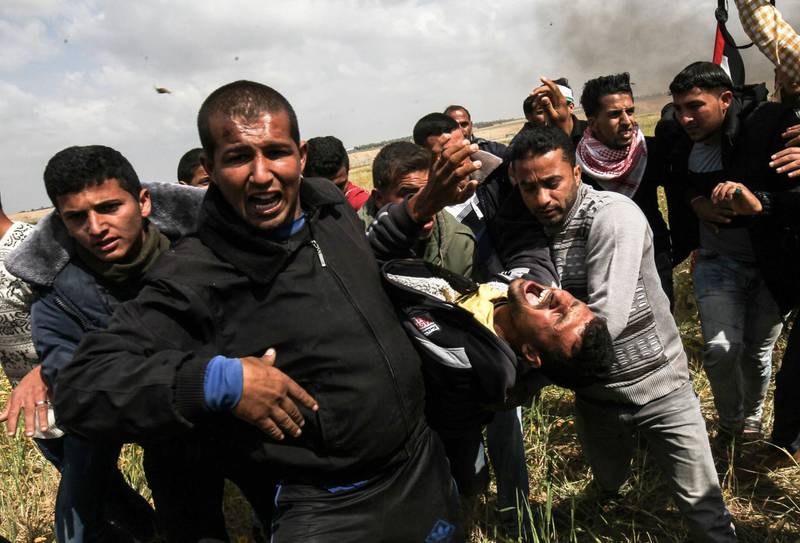 Faris al-Raqib (front-L), a member of the Islamic Jihad movement, who was later shot in the stomach and died of his wounds, is seen carrying an injured Palestinian man as they run for cover during clashes with Israeli security forces following a demonstration commemorating Land Day near the border with Israel, east of Khan Yunis, in the southern Gaza Strip on March 30, 2018.
Raqib, succumbed to his wounds on April 2, three days after being shot by Israeli forces when a mass protest led to clashes, Gaza's health ministry said, raising the death toll. / AFP PHOTO / SAID KHATIB