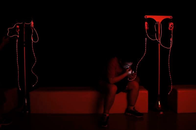 A man browses his smartphone while charging it by an art installation titled E Blood Bag.