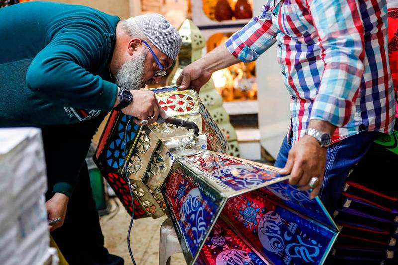 An elderly man seals the parts of a lantern as Palestinian craftsman Issam Zughair (unseen) holds it up, in his shop in the old city of Jerusalem on May 2, 2019. In his shop in Jerusalem's Old City, Zughair makes traditional lanterns for Muslims marking the holy month of Ramadan, battling competition from cheap Chinese imports. The shop boasts a mix of large and small lamps on show, some hanging from the ceiling while others are displayed outside to draw the attention of passers-by during the lively Ramadan evenings. / AFP / AHMAD GHARABLI
