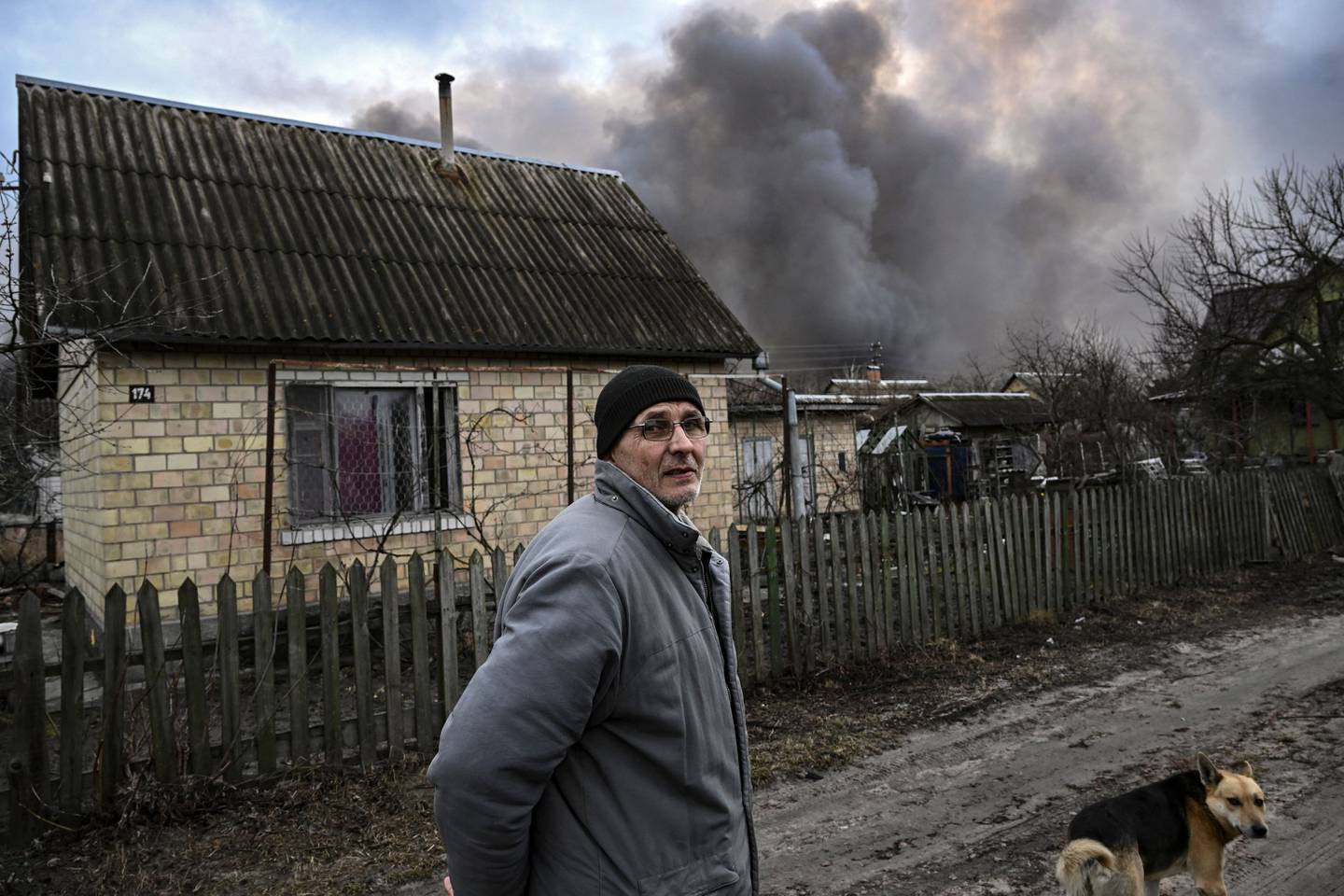 A man looks on in a street in Stoyanka, Ukraine, with smoke billowing from a house in the background.  AFP