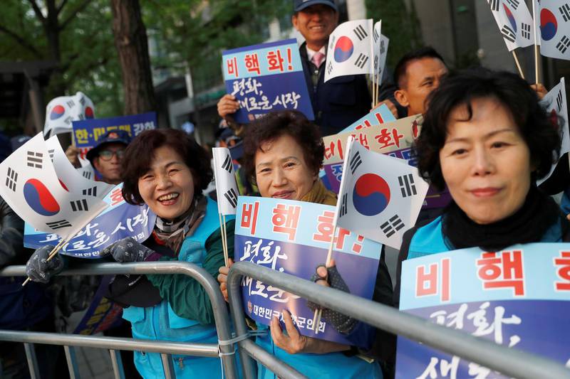 Supporters hold South Korean flags and signs while waiting for a convoy transporting South Korean President Moon Jae-in to the Korean summit.
