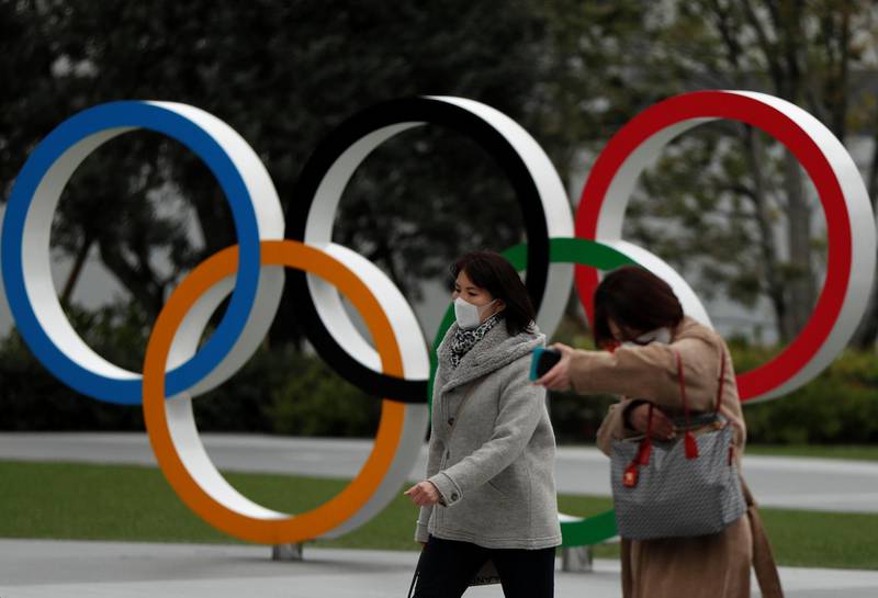 Passersby wearing protective face masks, following an outbreak of the coronavirus disease (COVID-19), walk past the Olympic rings in front of the Japan Olympics Museum, in Tokyo, Japan March 30, 2020. REUTERS/Issei Kato