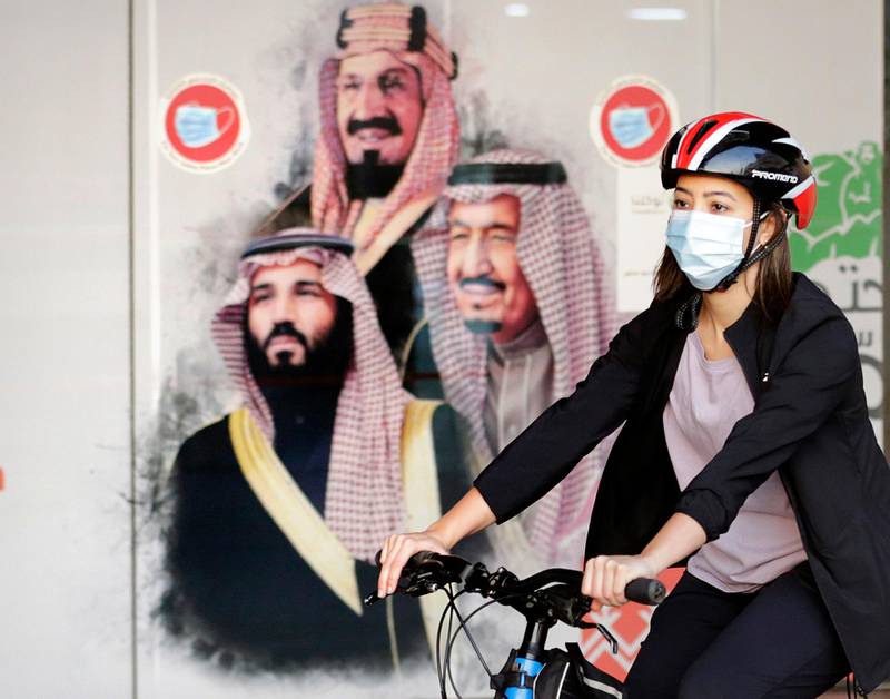 Sawsan Abdel Fattah, a Saudi cyclist and member of the Brave team, rides past a banner depicting King Salman, Crown Prince Mohammed bin Salman, and Saudi Arabia's founder King Abdulaziz, in Jeddah. AP