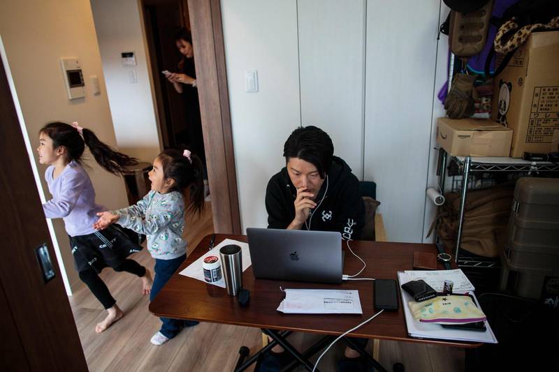 This picture taken on March 23, 2020 shows Yuki Sato, an employee in a startup company, working from home as a result of the COVID-19 novel coronavirus in Tokyo, as his daughters Yurina (L) and Hinano play and his wife Hitomi uses a mobile phone. / AFP / Behrouz MEHRI
