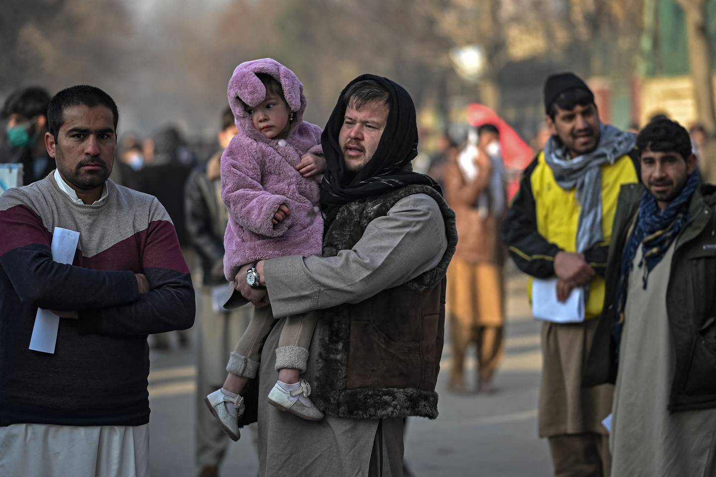 A man carries his daughter as people queue to enter the passport office at a checkpoint in Kabul on December 19, after Afghanistan's Taliban authorities said they will resume issuing passports. AFP