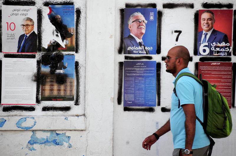 A man walks past candidates' posters and designated numbers a day before the start of presidential election in Tunis, Tunisia.