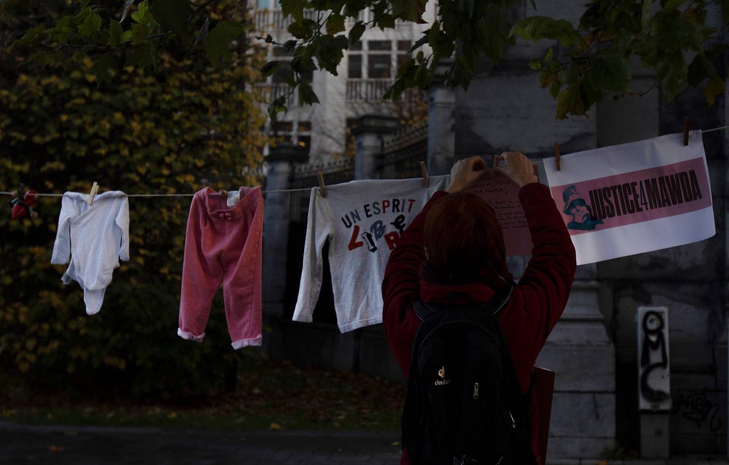 A woman hangs a piece of children's clothing on a line during a solidarity event for Mawda Shawri at the courthouse in Brussels, Monday, Nov. 23, 2020. A trial opened on Monday in the shooting death of two-year old toddler, Mawda Shawri, who was in a van during a high-speed chase between police and suspected migrant smugglers seeking to get to Britain. At the trial in Belgium's southern Mons, a policeman stands accused of involuntary manslaughter and two other men for being suspected migrant smugglers. (AP Photo/Virginia Mayo)