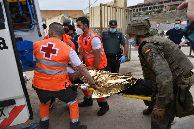 Red Cross members and Spanish soldiers carry a migrant into an ambulance. AFP