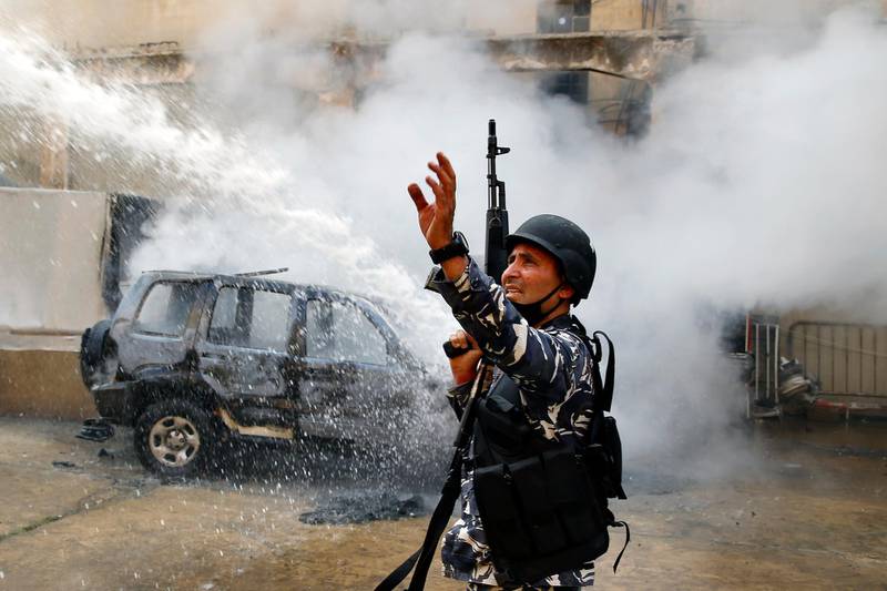 A police officer gestures to firefighters as they extinguish a police car that was set on fire by anti-government protesters, in the northern city of Tripoli, Lebanon, Tuesday, April 28, 2020. Hundreds of angry Lebanese took part Tuesday in the funeral of a young man killed in riots overnight in Tripoli that were triggered by the crash of Lebanon's national currency that sent food prices soaring. (AP Photo/Bilal Hussein)