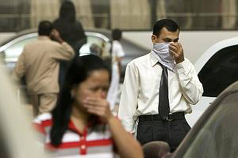 People cover their noses and mouths during a sandstorm that left a layer of dust over cars in Abu Dhabi.