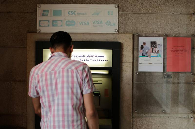 FILE - In this July 24, 2019 file photo, a man stands in front of an ATM machine outside a branch of the International Bank for Trade and Finance, in Damascus, Syria. The Syrian pound has hit a record low amid the countryâ€™s grinding war and as a financial and political crisis roils neighboring Lebanon, Syriaâ€™s economic lung. The dollar was worth 920 Syrian pounds at some exchange shops on Monday, Dec. 2, 2019, in the capital, Damascus, a sharp drop from recent days. (AP Photo/Hassan Ammar, File)