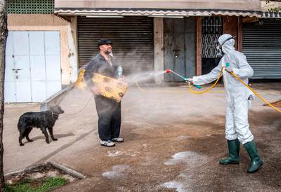 TOPSHOT - A Moroccan health ministry worker disinfects a man walking a dog and carrying a mat in the capital Rabat on March 22, 2020. A public health state of emergency went into effect in the Muslim-majority country late on March 20, and security forces and the army have been deployed on the streets to combat the spread of COVID-19 coronavirus disease. People have been ordered to stay at home, and restrictions on public transport and travel between cities are also in place. / AFP / FADEL SENNA
