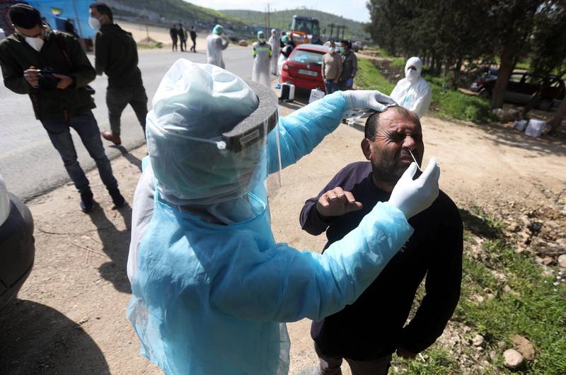 An employee of the Palestinian health ministry collects a swab sample from a worker crossing back from Israel at the checkpoint of Tarqumiya, near the West Bank town of Hebron.  EPA