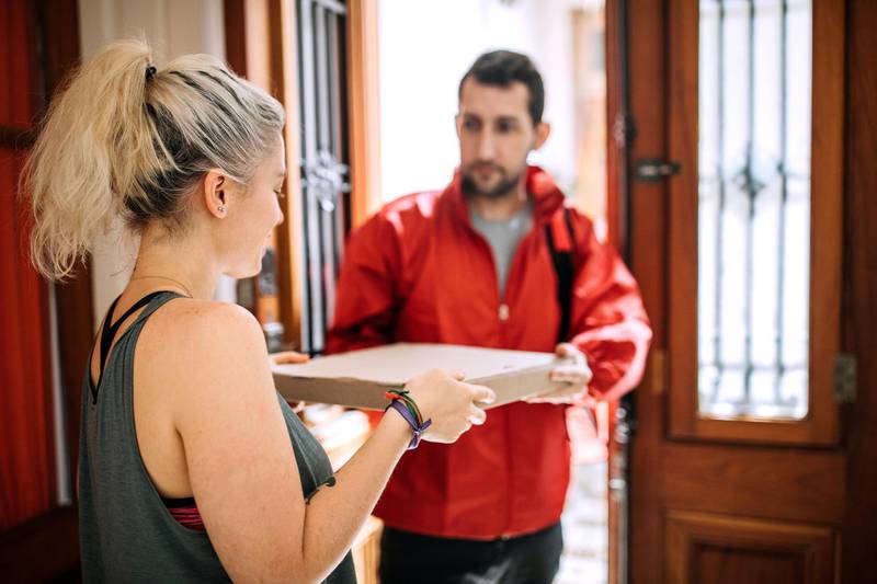 Delivery person giving Pizza box to woman at doorstep