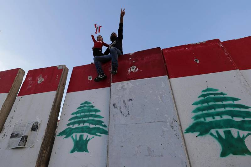An anti-government protester and his daughter stand on a concrete wall installed by authorities to keep protesters far from the main Lebanese government headquarters and open the road to parliament, in downtown Beirut, Lebanon. AP Photo