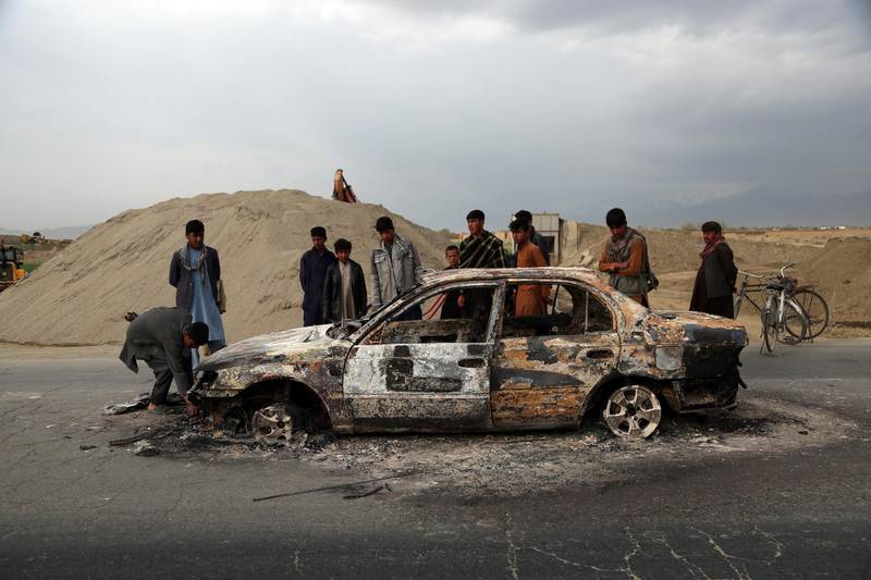 FILE - In this April 9, 2019, file photo, Afghans watch a civilian vehicle burnt after being shot by U.S. forces following an attack near the Bagram Air Base, north of Kabul, Afghanistan. Three American service members and a U.S. contractor were killed when their convoy hit a roadside bomb on Monday near the main U.S. base in Afghanistan, the U.S. forces said. The Taliban claimed responsibility for the attack. Intelligence alleging that Afghan militants might have accepted Russian bounties for killing American troops didnâ€™t scuttle the U.S.-Taliban agreement or President Donald Trumpâ€™s plan to withdraw thousands more troops from the war. (AP Photo/Rahmat Gul, File)