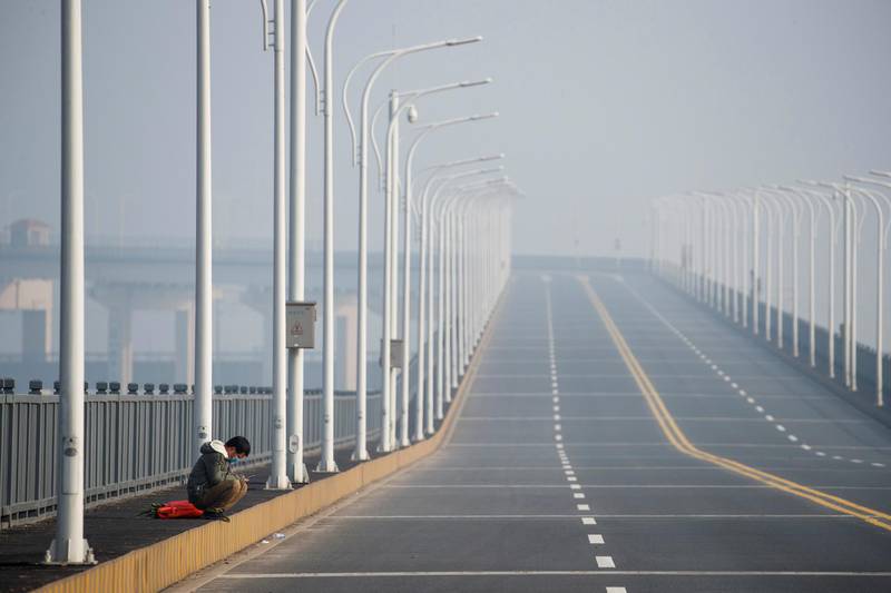 A man who arrived from Hubei province sits near a checkpoint after being refused entry at the Jiujiang Yangtze River Bridge in Jiujiang, Jiangxi province, China, as the country is hit by an outbreak of a new coronavirus. Reuters