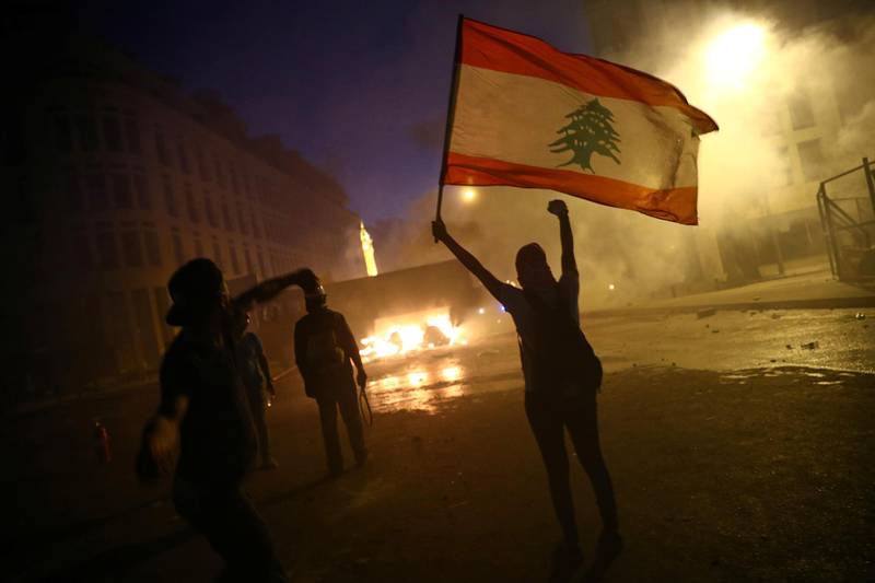 A demonstrator holds a Lebanese flag as another hurls stones during. Reuters